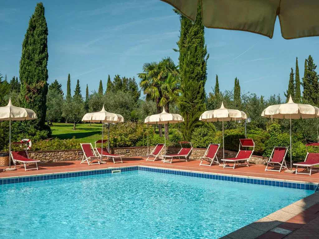  La piscina esterna con lettini e ombrelloni, tra cipressi e ulivi