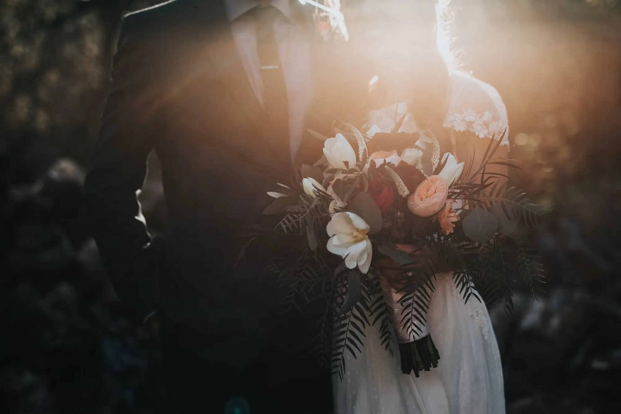 Coppia di sposi all'aperto controluce al tramonto con un bellissimo bouquet